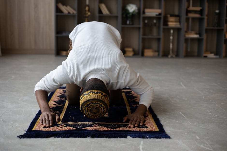 A man worships indoors, performing Islamic prayer on a mat.