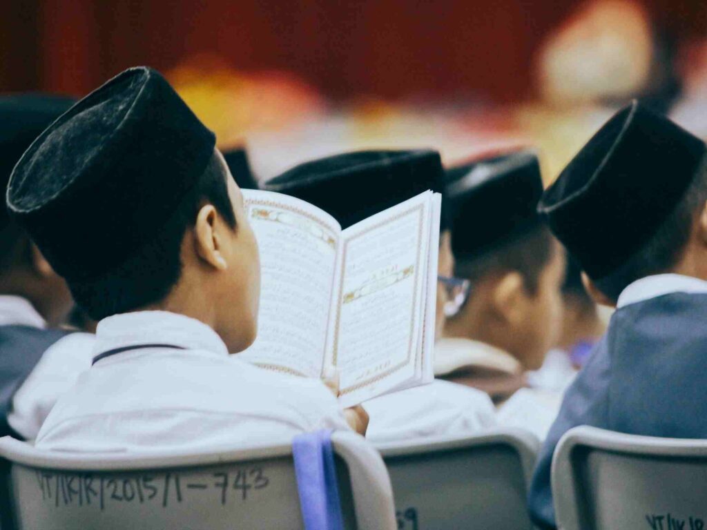 Boys in traditional attire reading the Quran during a religious gathering, showcasing faith and devotion.