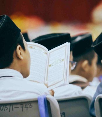 Boys in traditional attire reading the Quran during a religious gathering, showcasing faith and devotion.